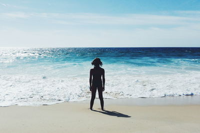 Rear view of man standing on beach against sky