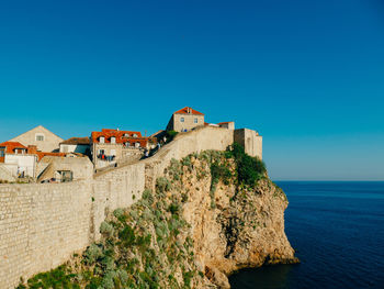 Buildings by sea against clear blue sky