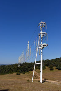 Electricity pylon on field against clear blue sky