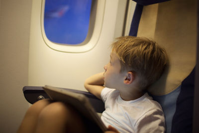 Boy looking away while sitting with digital tablet in airplane