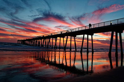 Silhouette pier at beach against sky during sunset