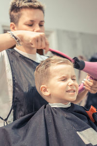 Female hairdresser styling boy hair in salon