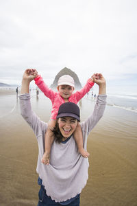 Happy mom gives daughter shoulder ride at cannon beach.