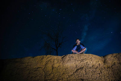 Low angle view of man sitting on rock formation against star field