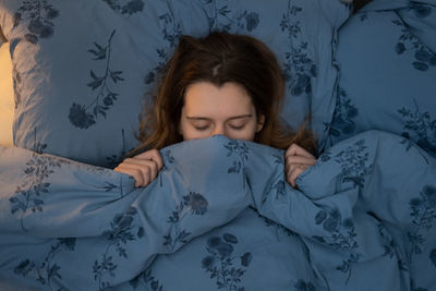 Attractive young caucasian girl sleeping in bed. woman wrapped up in a blanket up to her nose.