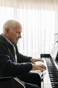 Senior man sitting in wheelchair playing piano at home