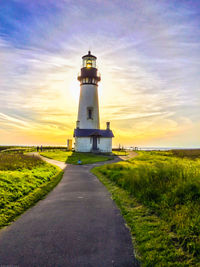 Lighthouse on road against cloudy sky