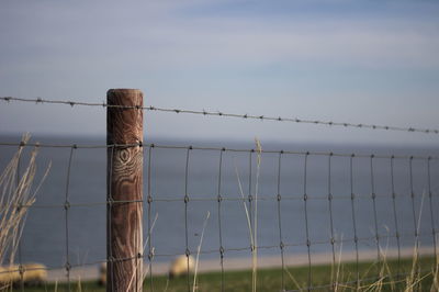 Close-up of barbed wire fence at beach against sky