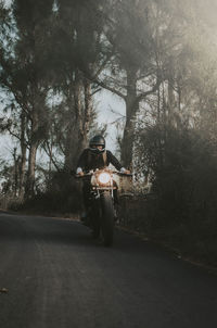 Man riding motorcycle on road against trees