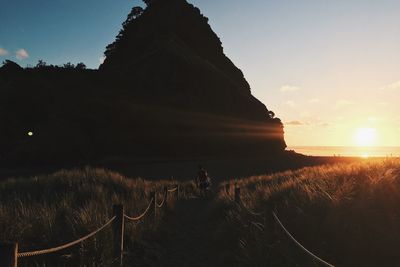 Rear view of man walking on footpath leading towards mountain at sunset