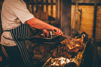 Side view of man preparing meat on barbecue