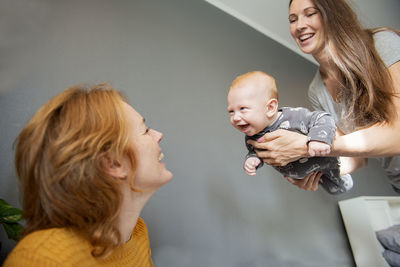 Grandmother and mother in living room playing with smiling newborn baby boy