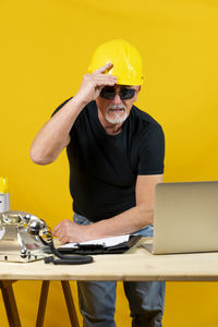 Engineer using laptop while sitting on table against yellow background