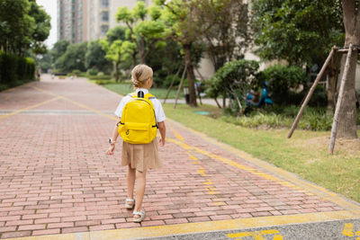 Rear view of girl walking on footpath in city