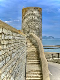 Low angle view of stone wall by sea against sky