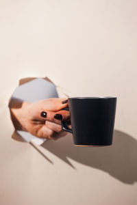 A hand holding a coffee mug through a torn paper background. copy space.