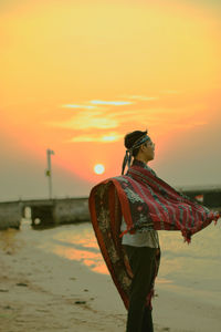 Woman standing on beach against sky during sunset