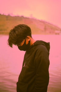 Young man standing against orange sky during sunset