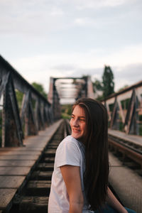 Portrait of smiling woman standing on footbridge against sky