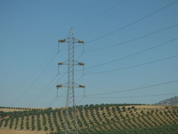 Low angle view of electricity pylon on field against clear sky