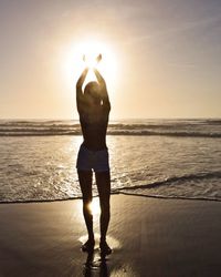 Rear view of man standing at beach during sunset