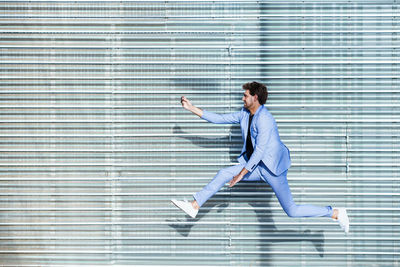 Full length of businessman jumping against wall outdoors