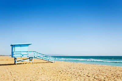 Lifeguard hut on beach against clear blue sky