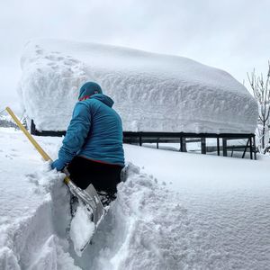 Rear view of man with shovel kneeling on snow covered land
