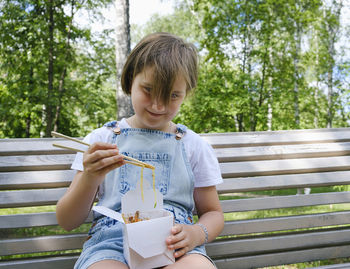 Teenage girl on a walk on a summer day in the park has lunch with noodles wok