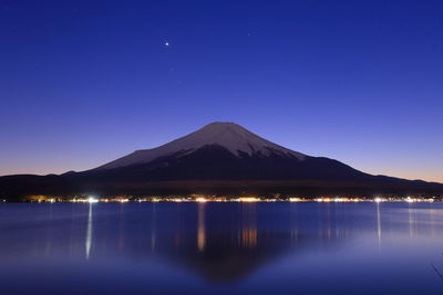 Scenic view of lake by mountains against clear blue sky at night