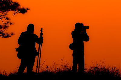 Silhouette man photographing against orange sky