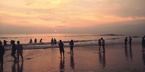 People at beach against sky during sunset