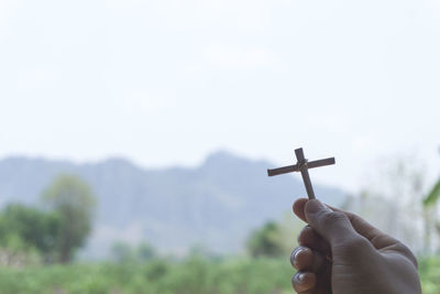 Hand holding cross against sky