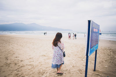 Rear view of woman standing on beach against sky