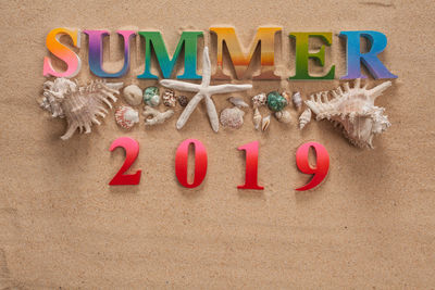 High angle view of summer text with numbers and seashells on sand at beach