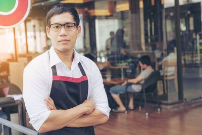 Portrait of waiter with arms crossed standing at restaurant