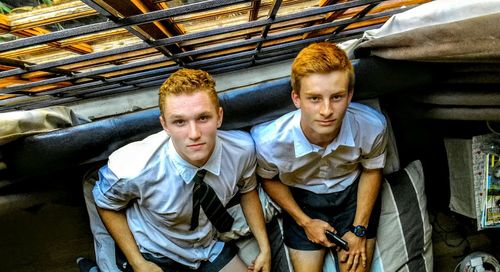 Portrait of young male friends sitting on sofa by window at home