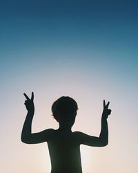 Silhouette boy gesturing while standing against sky