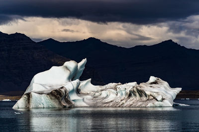 Scenic view of a gigantic iceberg in a frozen lake against mountain range