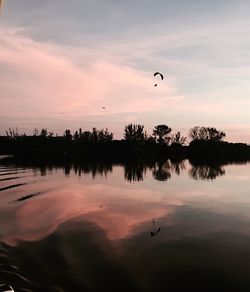 Silhouette of man flying over lake against sky during sunset