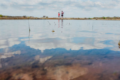 Reflection of woman in lake against sky