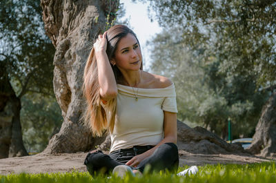 Young woman sitting on tree trunk against plants