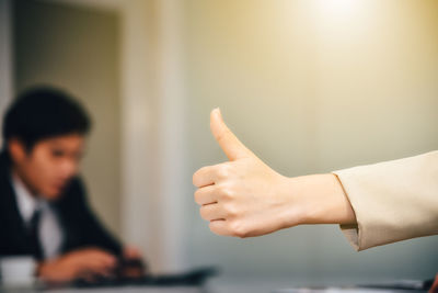 Cropped hand of businesswoman gesturing thumbs up while colleague working at office
