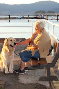 Full length of woman sitting by lake with golden retriever on bench