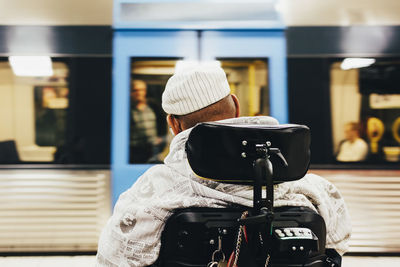 Rear view of disabled man sitting on wheelchair against train at station