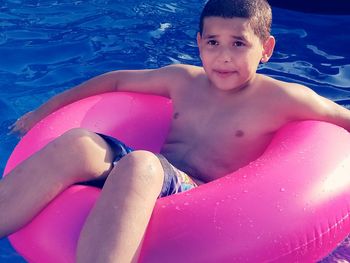 Portrait of shirtless boy on inflatable ring in swimming in pool