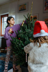 Two girls decorating green christmas tree in their home