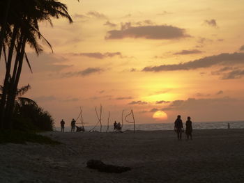 Silhouette people on beach against sky during sunset