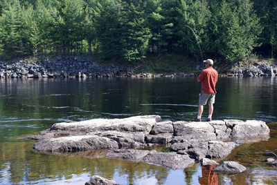 Rear view of man standing on rock by lake