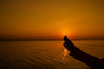 Optical illusion of cropped hand holding light bulb against sun during sunset